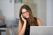 Jeune femme souriante téléphonant devant un ordinateur portable