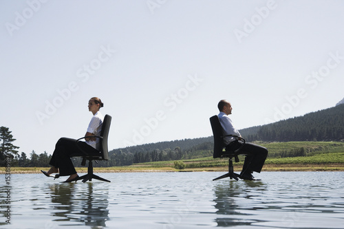 Photo: Businessman and woman in office chairs on water facing away Businessman and woman in office chairs on water facing away