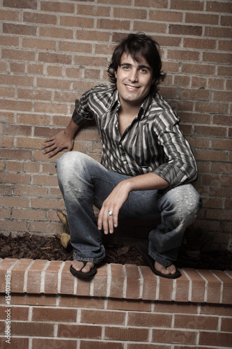 Photo: Handsome man squatting on a building garden ledge Handsome man squatting on a building garden ledge