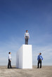 Businessman standing on wall outdoors with two men watching