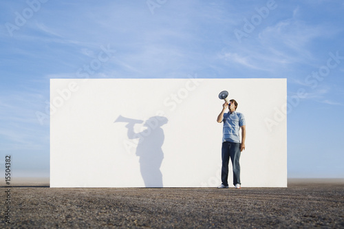 Photo: Man standing in front of wall outdoors with megaphone and shadow Man standing in front of wall outdoors with megaphone and shadow
