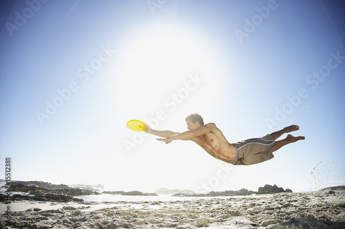 Photo: A man leaping through the air at the beach catching a Frisbee A man leaping through the air at the beach catching a Frisbee