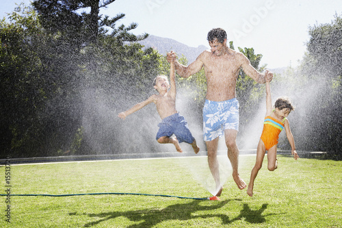 Photo: a father playing with his children in a sprinkler a father playing with his children in a sprinkler