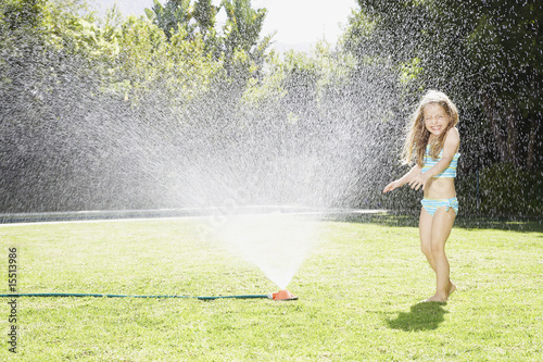 Photo: A young girl playing in a sprinkler A young girl playing in a sprinkler