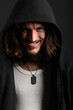Young man in black hood with cheeky grin on black background