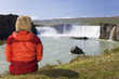 Woman Sitting At Godafoss Waterfall In Iceland