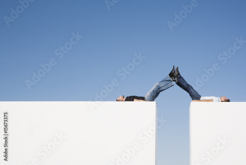 Photo: Two men atop two walls with their legs up Two men atop two walls with their legs up