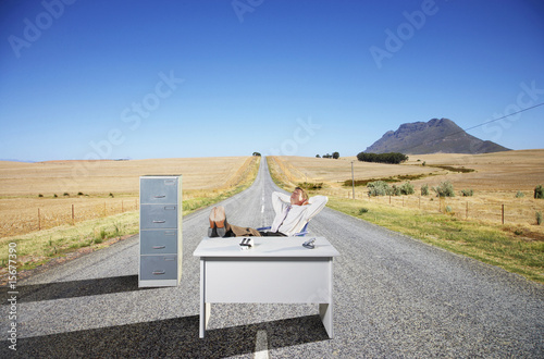 Photo: A businessman in the middle of the road at his desk A businessman in the middle of the road at his desk