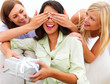 Friends covering a happy girl's eyes while holding a gift