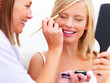Friend applying makeup to a smiling young girl isolated on white