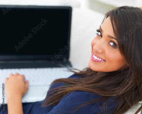 Photo: Young woman sitting on sofa using laptop Young woman sitting on sofa using laptop