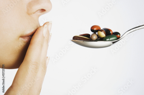 Photo: Woman with hand to mouth blocking spoonful of pills Woman with hand to mouth blocking spoonful of pills