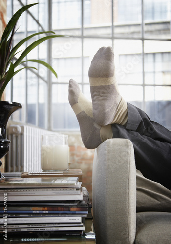 Photo: Man's feet up on arm of couch in modern home Man's feet up on arm of couch in modern home