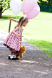 Little girl at a park with balloons and a little brown teddy.
