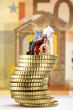 Figurine in wheelchair and caregiver on pile of coins