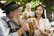 Foto: Germany, Bavaria, Upper Bavaria, Bavarian man and Asian woman in beer garden raising stein glasses, portrait Germany, Bavaria, Upper Bavaria, Bavarian man and Asian woman in beer garden raising stein glasses, portrait