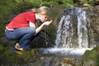 Young woman drinking water from stream, side view