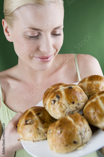 Photo: oung woman holding a plate of hot cross buns, smiling oung woman holding a plate of hot cross buns, smiling