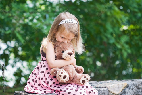 Photo: Adorable little girl giving her teddy bear a kiss on the head. Adorable little girl giving her teddy bear a kiss on the head.