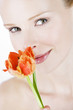 A portrait of a young woman smelling an orange tulip, close-up