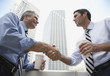 Two businessmen outdoors on a balcony shaking hands holding coffee cups