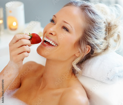 Foto: Happy young female eating a strawberry while in a bath tub Happy young female eating a strawberry while in a bath tub