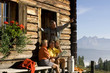 Mature couple sitting in front of alpine hut, talking to farmer