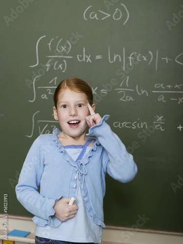 Photo: Girl (6-7) standing by blackboard, solving arithmetic problem Girl (6-7) standing by blackboard, solving arithmetic problem