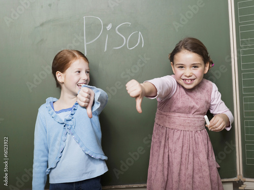 Foto: Girls (4-7) standing by blackboard smiling, showing thumbs down sign Girls (4-7) standing by blackboard smiling, showing thumbs down sign