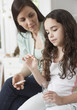 Woman helping young girl take medicine in bedroom