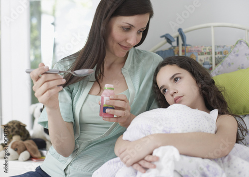 Photo: Woman helping young girl take medicine in bedroom Woman helping young girl take medicine in bedroom