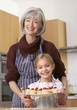 Woman and young girl in kitchen holding plate of cherry cupcakes and smiling
