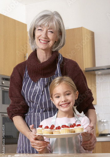 Photo: Woman and young girl in kitchen holding plate of cherry cupcakes and smiling Woman and young girl in kitchen holding plate of cherry cupcakes and smiling
