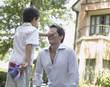 Man outdoors with young boy covering his eyes and hiding gift behind his back