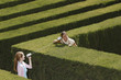 Friends using tin can telephone in hedge maze