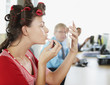 Businesswoman in curlers applying lipstick at desk