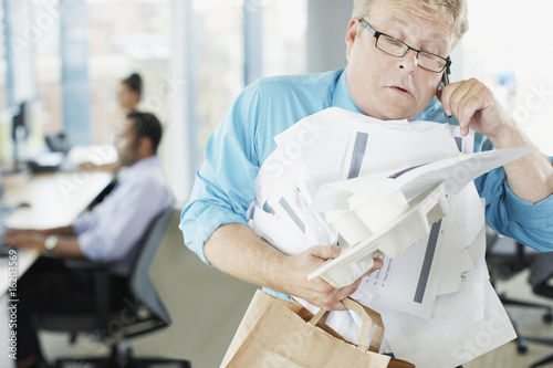 Photo: Businessman talking on phone holding paperwork and coffee Businessman talking on phone holding paperwork and coffee
