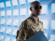 Man in camouflage holding folder near bank of computers