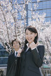 桜の花の前に立つスーツ姿の女性と男性