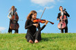 violinist and two violoncellists play on grass against sky violinist and two violoncellists play on grass against sky