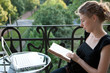Foto: junge blonde Frau sitzt vor Laptop und liest Buch auf Balkon junge blonde Frau sitzt vor Laptop und liest Buch auf Balkon