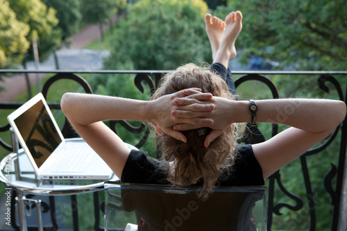 Foto: junge blonde Frau entspannt, Füße hoch, vor Laptop auf Balkon junge blonde Frau entspannt, Füße hoch, vor Laptop auf Balkon