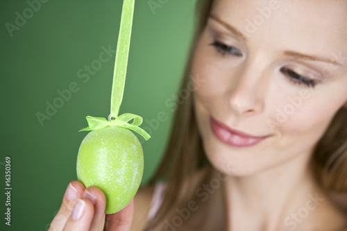 Photo: A young blonde woman holding a green Easter egg, close-up A young blonde woman holding a green Easter egg, close-up
