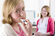 Worried girl holding thermometer in mouth with nurse in background