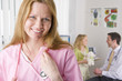 Nurse in office smiling with doctor and girl in background