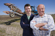 Foto: Farmers standing with arms crossed in field with tractor and plough in background Farmers standing with arms crossed in field with tractor and plough in background