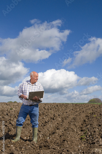 Photo : Farmer using laptop in ploughed field Farmer using laptop in ploughed field