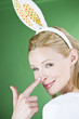 A young blonde woman wearing rabbit ears, touching her nose