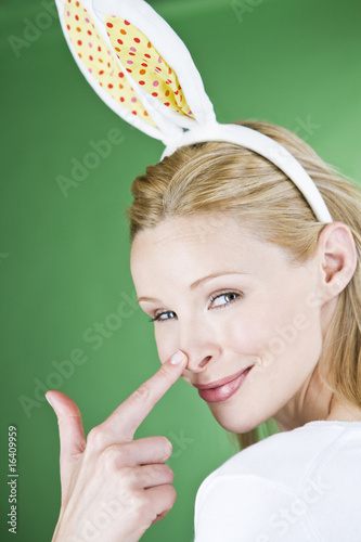Photo: A young blonde woman wearing rabbit ears, touching her nose A young blonde woman wearing rabbit ears, touching her nose