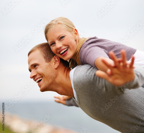 Photo: Pretty woman being carried on a man's back, hands outstretched Pretty woman being carried on a man's back, hands outstretched